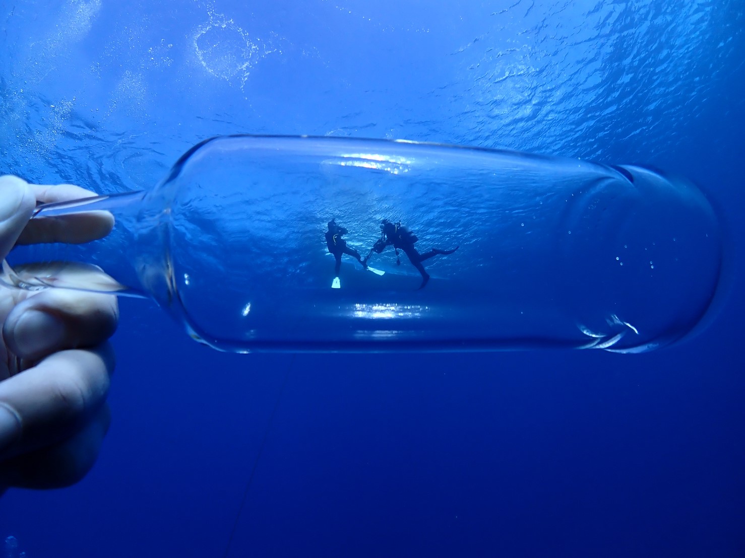 水中で遠近法を使って透明の空き瓶の中に2人のダイバーを写している